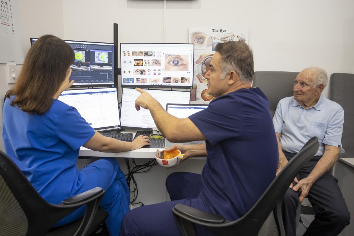 Ophthalmology team reviewing eye scans with an older patient in an eye clinic